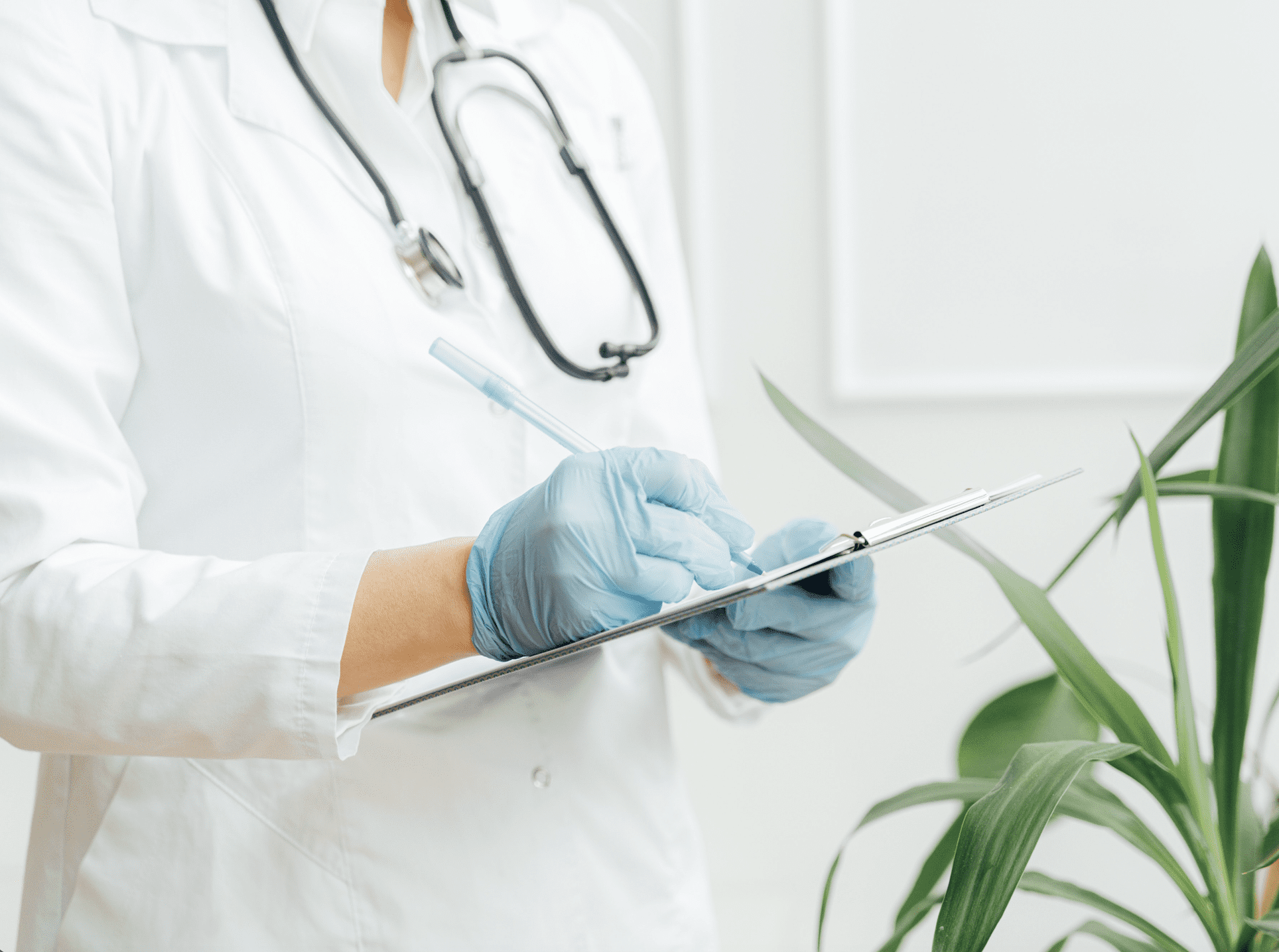 A doctor, wearing blue hygiene gloves, is writing in a patient file.
