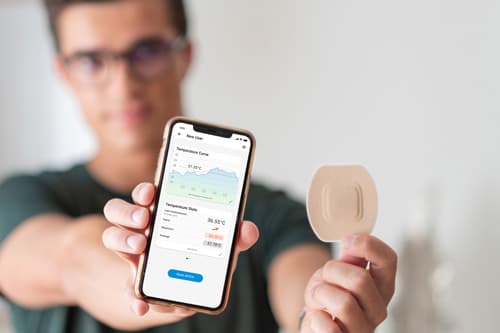Junge mit Brille hält sein Smartphone mit geöffneter STEADYTEMP® App und den STEADYTEMP® Patch in die Kamera